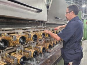 Man wearing black is working on a line of gold colored large cable attachments