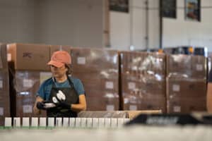 Woman with red cap works on a factory line of white deodorant containers.