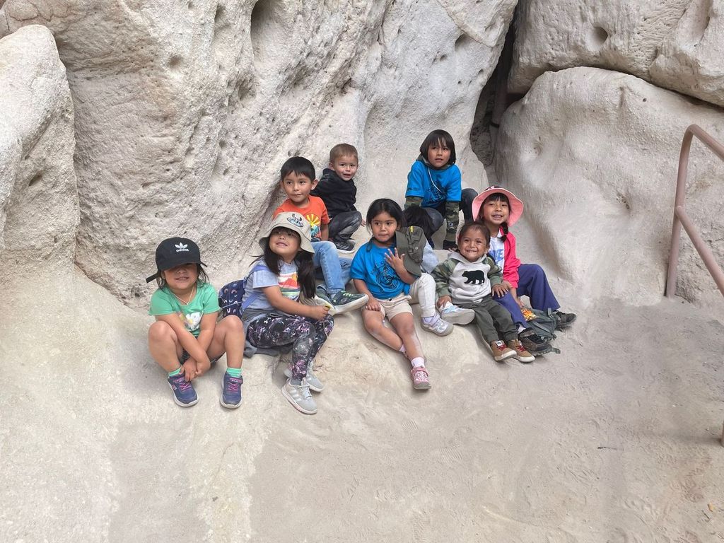 8 children sit on white rock formation at Bandelier National Monument