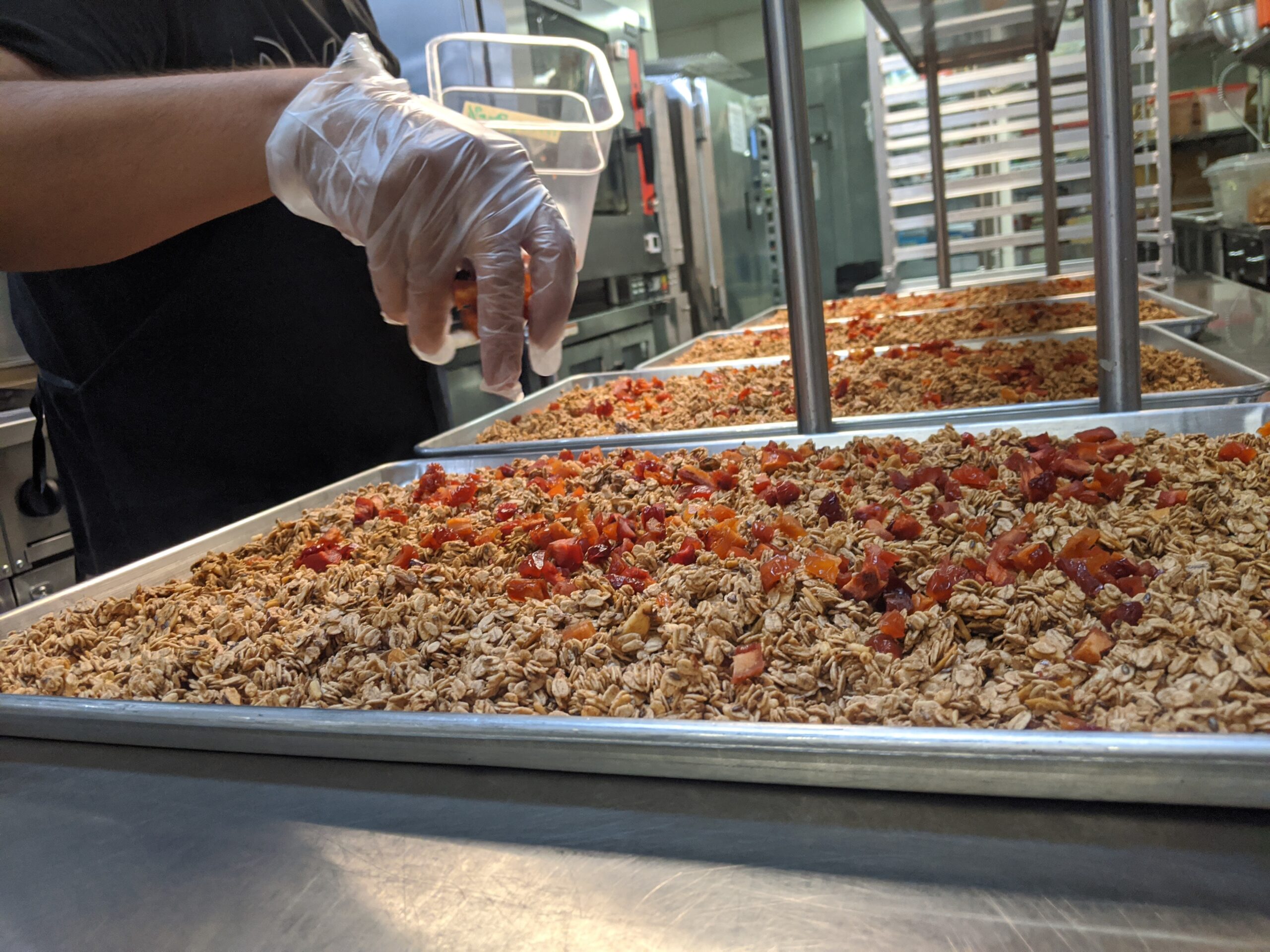 Kitchen worker inspects a pan of freshly made granola