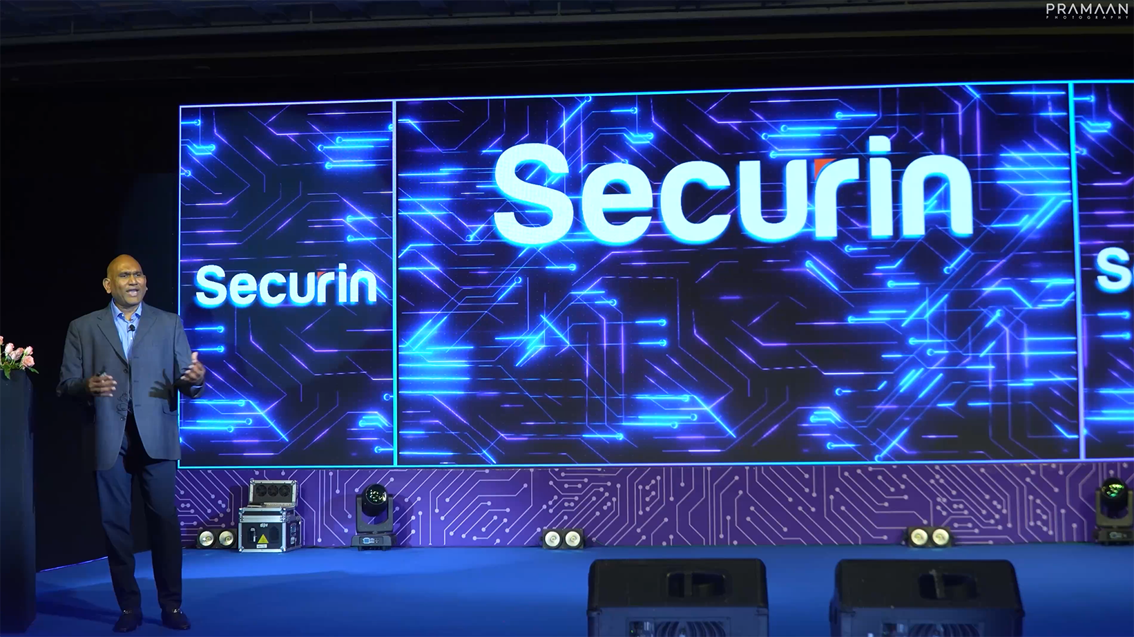 Presentation by a man in a suit standing in front of a large digital screen with Securin company logo.