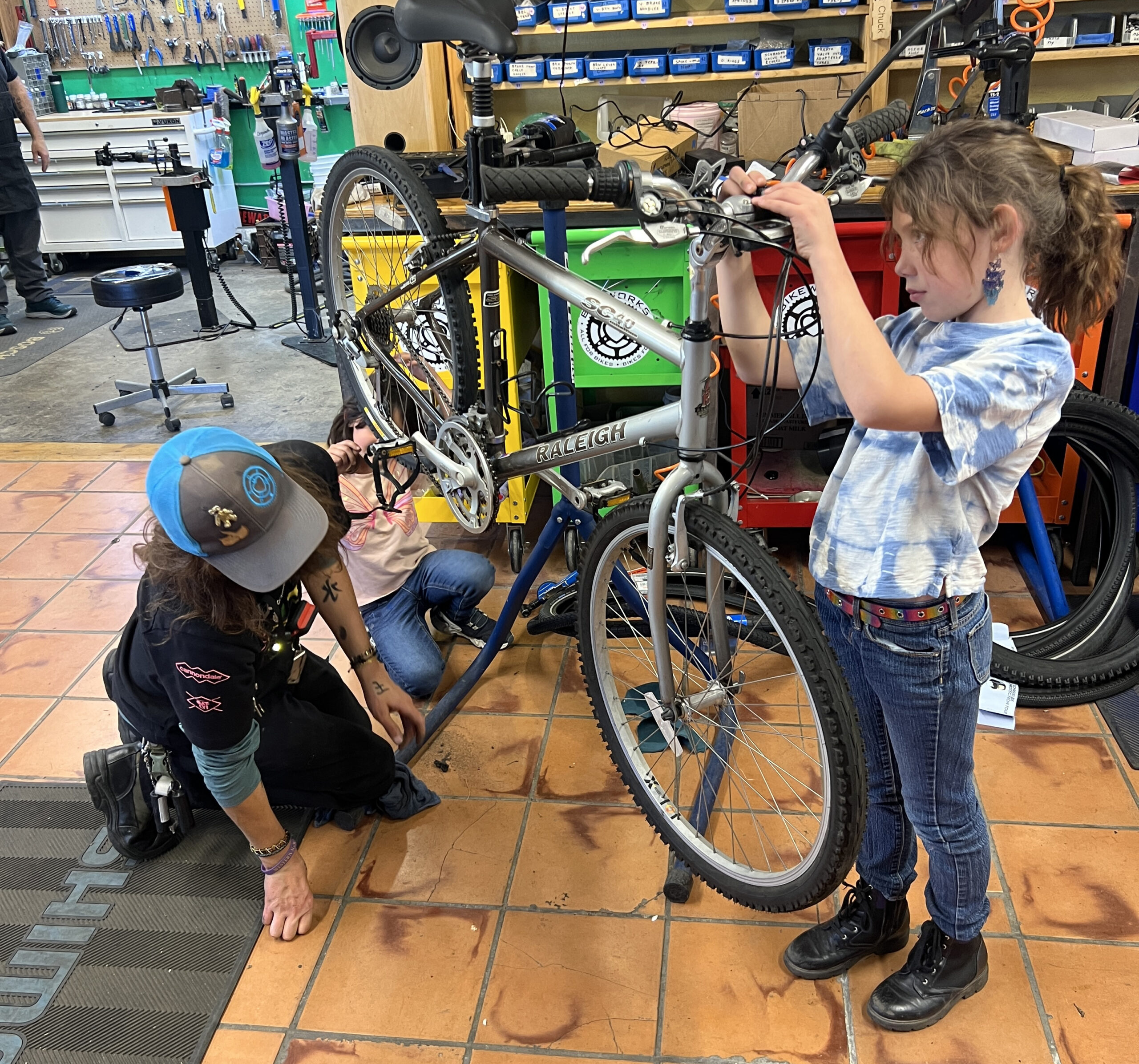 Three young people in a bike shop are looking at a bicycle that is up on a repair stand.