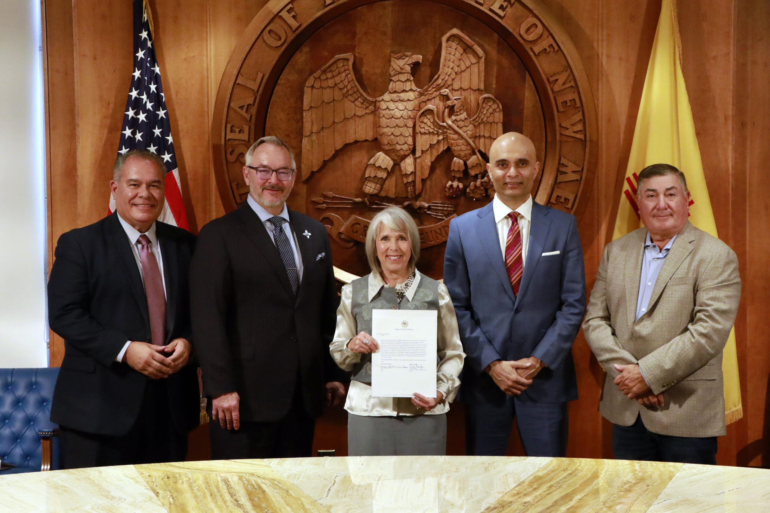 Governor Michelle Lujan Grisham stands center with a copy of the MOU in hand, flanked by state and company dignitaries with Sec Rob Black to her left.